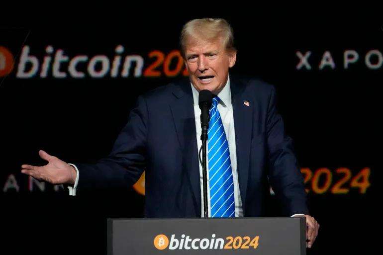 Donald Trump speaking at a podium with Bitcoin 2024 branding, gesturing with his hands.